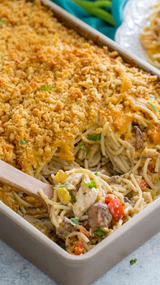 Side shot of chicken spaghetti casserole in a backing dish with a wooden spoon inside.