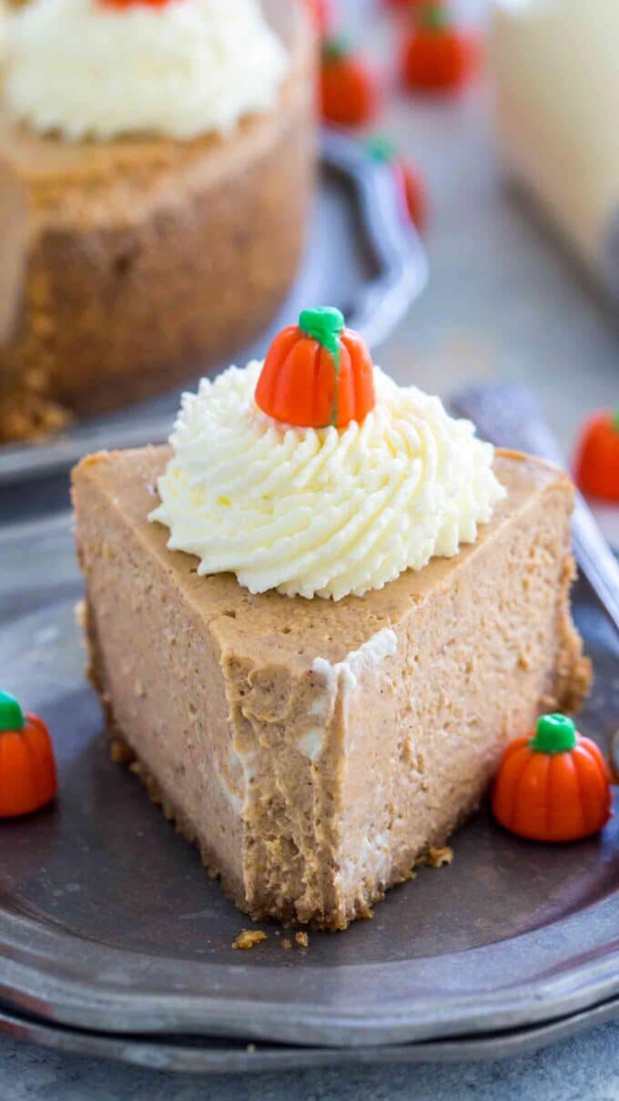 a slice of pumpkin cheesecake topped with whipped cream and candy pumpkin