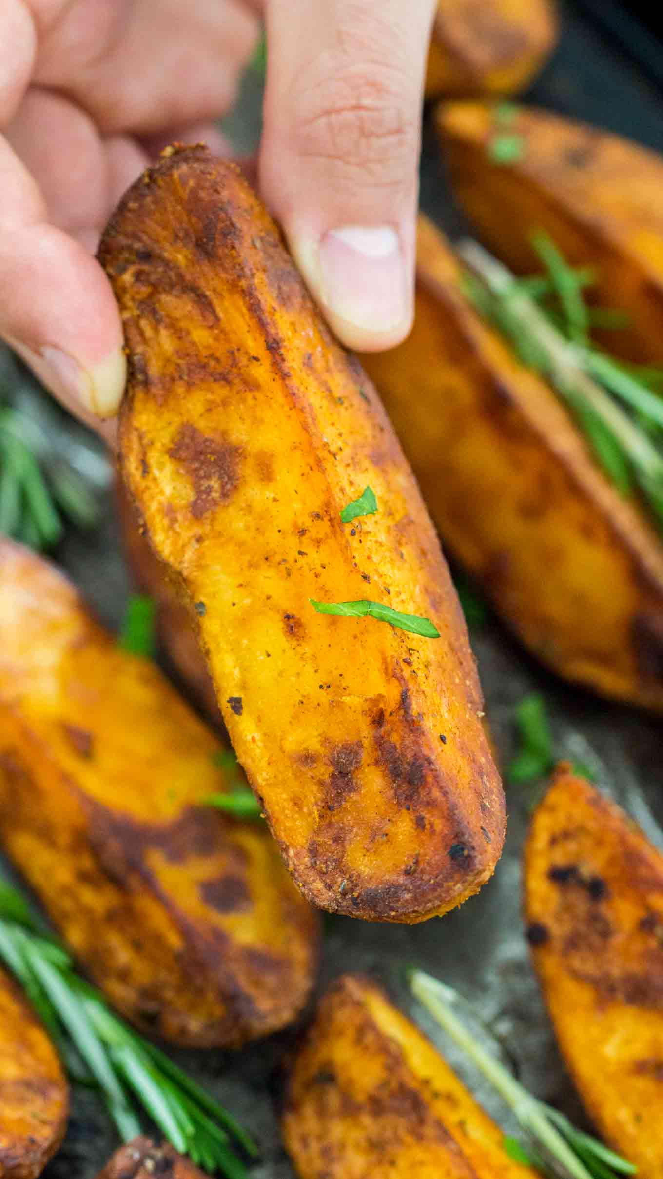 a hand holding a thick and crispy roasted rosemary potato