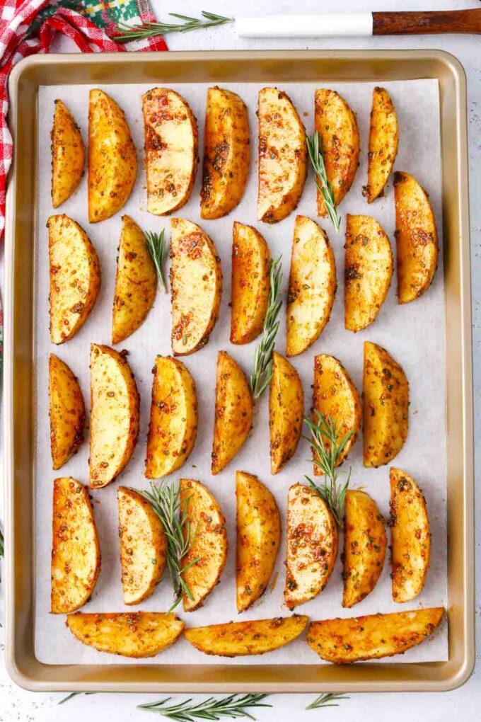 potato wedges covered in a rosemary paprika sauce arranged on a baking sheet