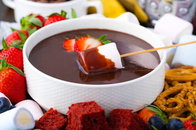 A bowl with crockpot chocolate fondue with a strawberry and marshmallow in it.