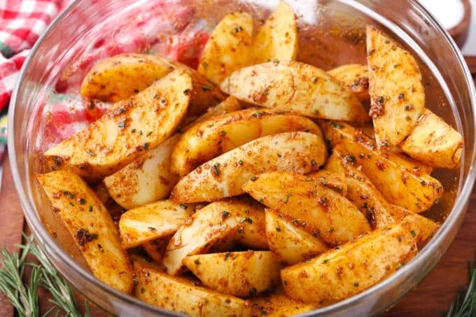 mixing potato wedges with rosemary paprika sauce in a bowl