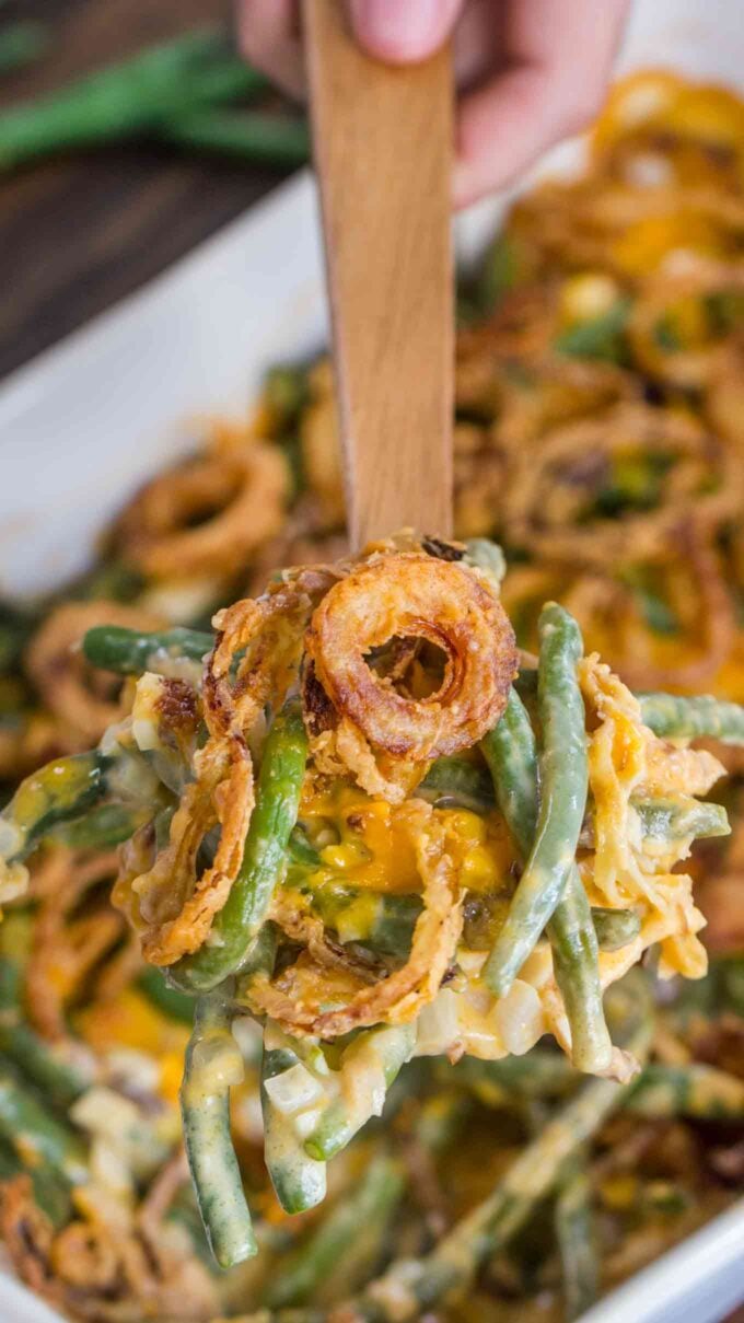 Creamy green bean casserole with French onion rings on a wooden spoon