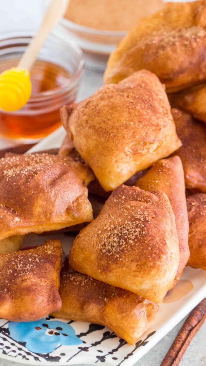 a pile of homemade sopapillas topped with cinnamon sugar and honey on the side