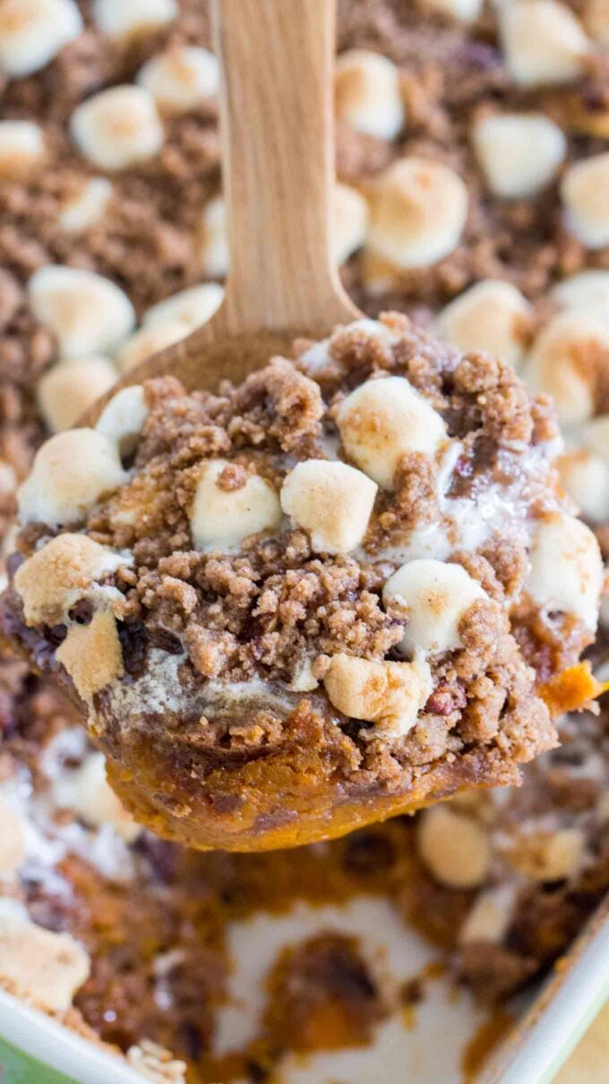 Sweet potato casserole topped with pecans and mini marshmallows on a wooden spoon