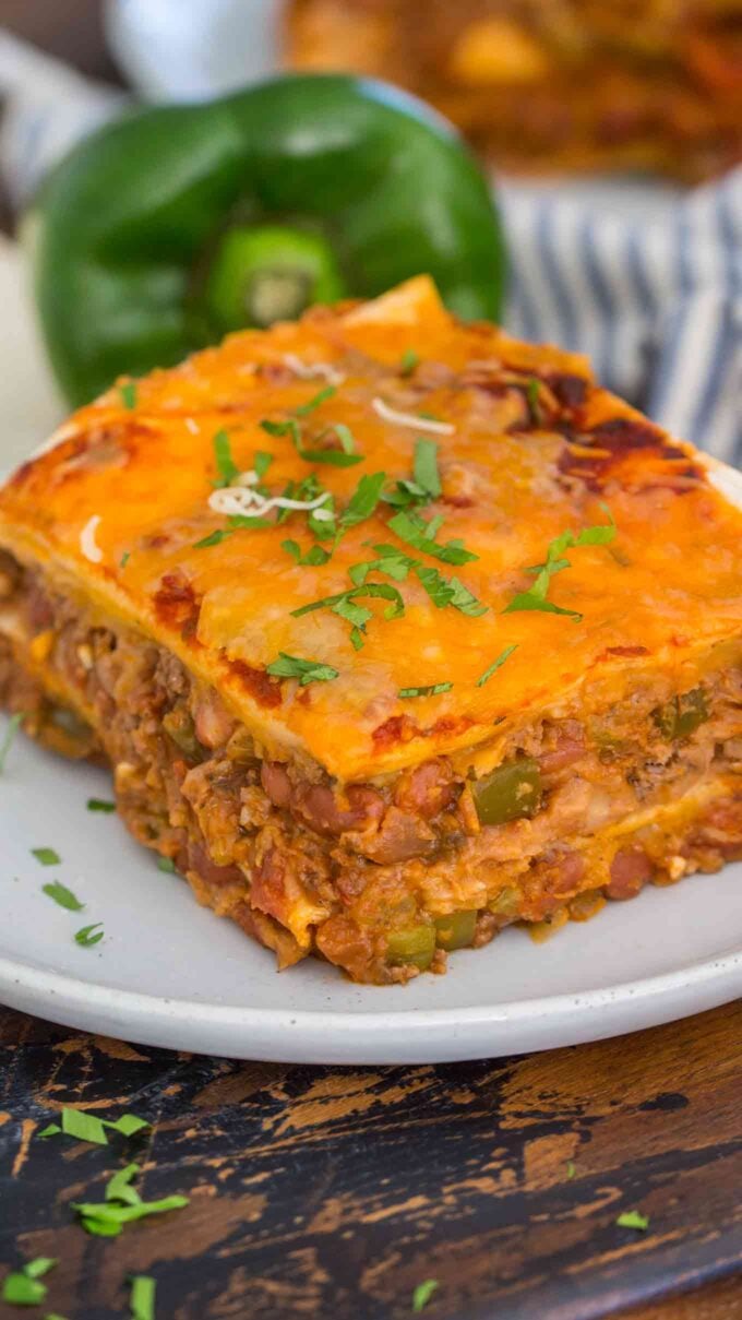 sliced taco lasagna on a white plate with a green bell pepper in the background