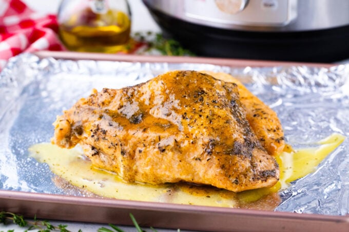A turkey breast that was cooked in the Instant Pot, placed on a baking sheet and covered in a butter mixture.