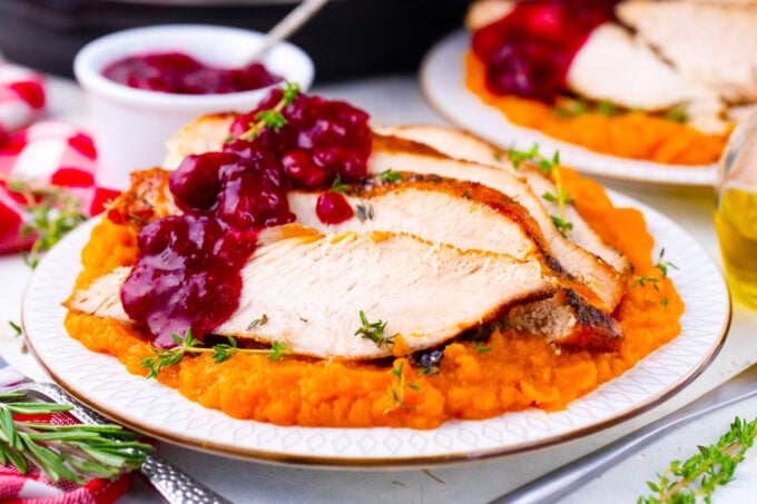 Sliced instant pot turkey breast served with cranberry sauce and mashed sweet potatoes.