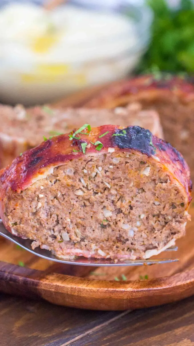 A slice of juicy meatloaf wrapped in bacon on a plate.