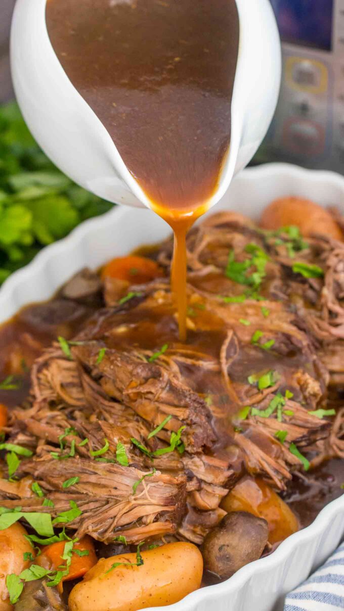 drizzling gravy sauce on top of pot roast with veggies and potatoes