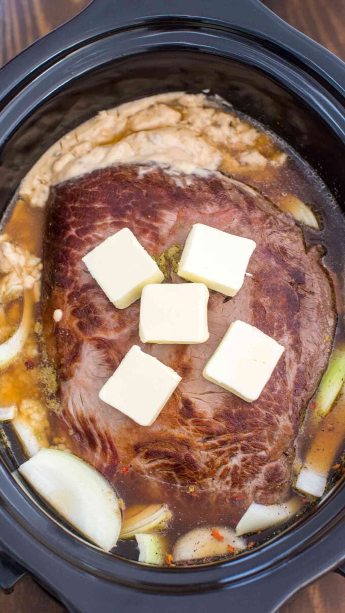 Picture of London broil beef cut in the crockpot topped with butter.