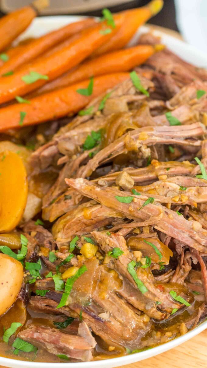 close shot of shredded cooked London broil with carrots and potatoes on a white plate.