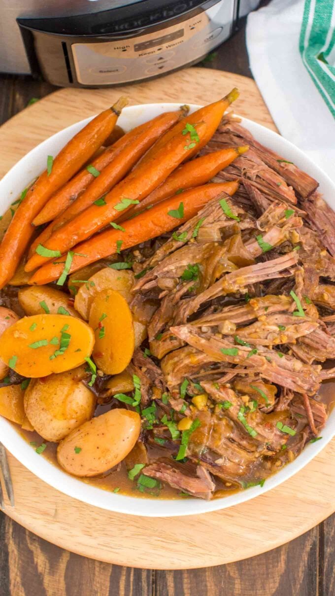 Image of slow cooker London broil with carrots and potatoes on a white plate.
