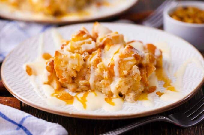 a slice of bread pudding with raising and cream cheese glaze on a plate