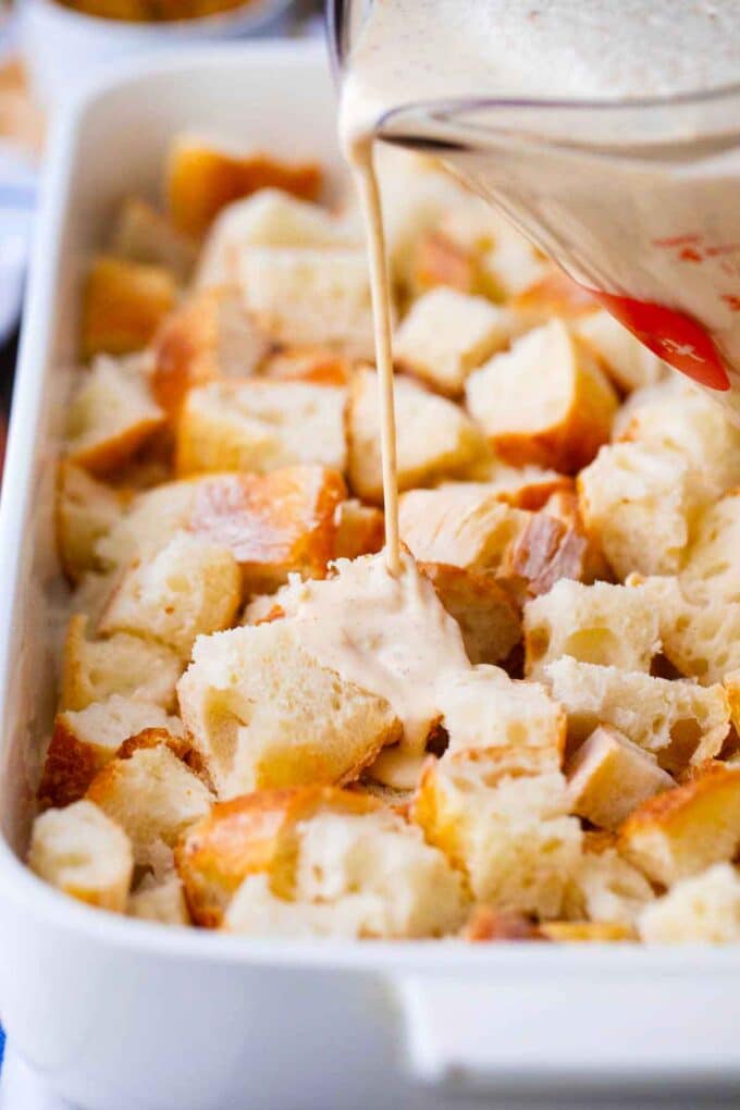 pouring milk mixture of top of bread cubes in a baking dish