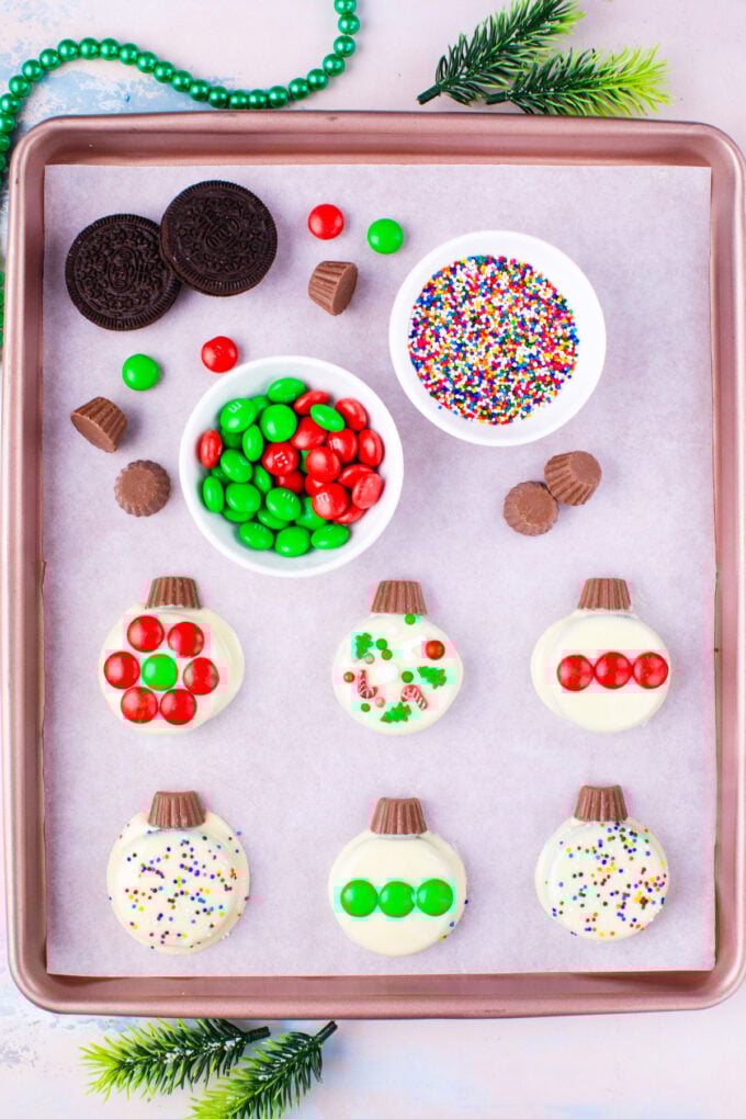 Christmas Oreo ornaments on a cookie sheet with candies and sprinkles.