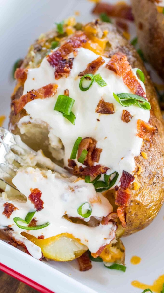 Loaded baked potato topped with sour cream, shredded cheese, green onion, and bacon bits.