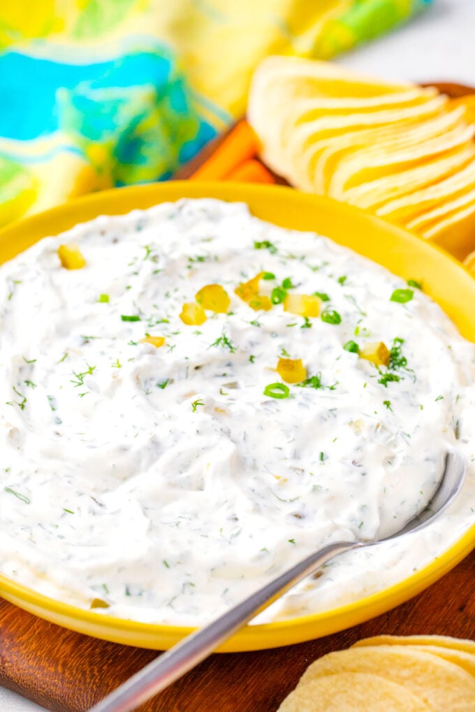 A bowl of creamy dill pickle dip with a serving spoon in it.