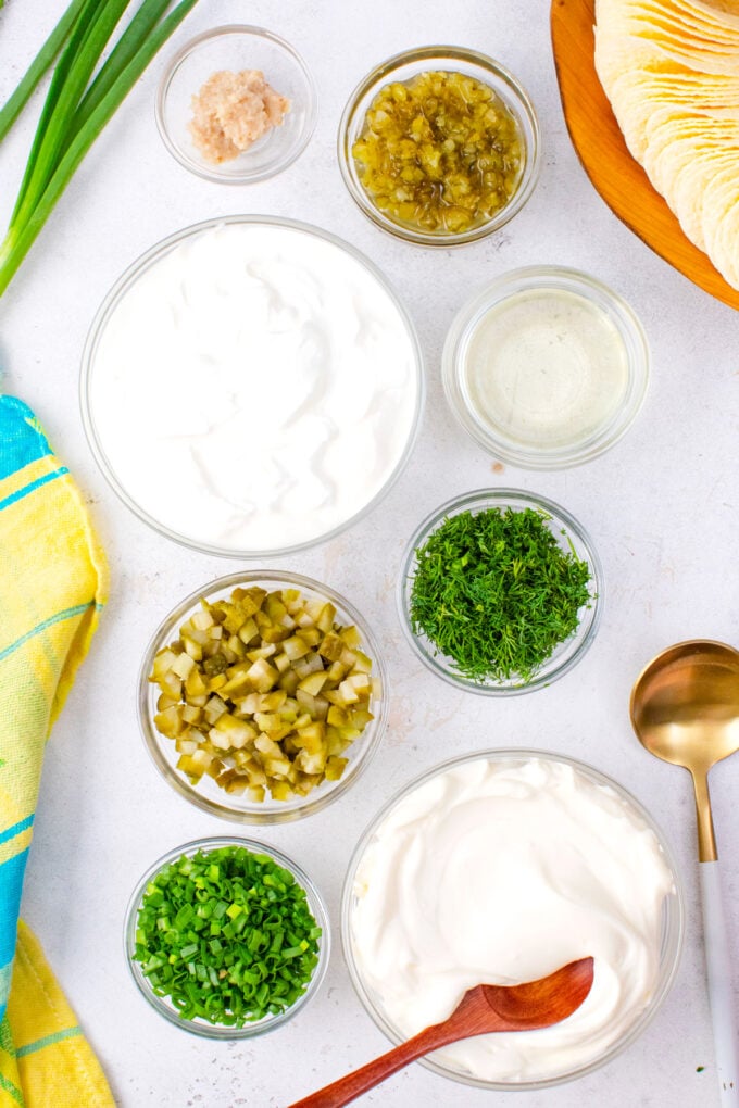 Overhead shot of dill pickle dip ingredients in bowls on a white surface.