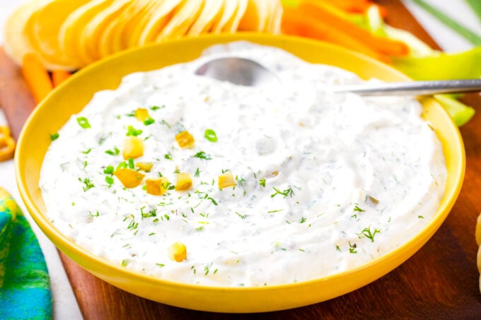 A bowl of dill pickle dip served with potato chips.