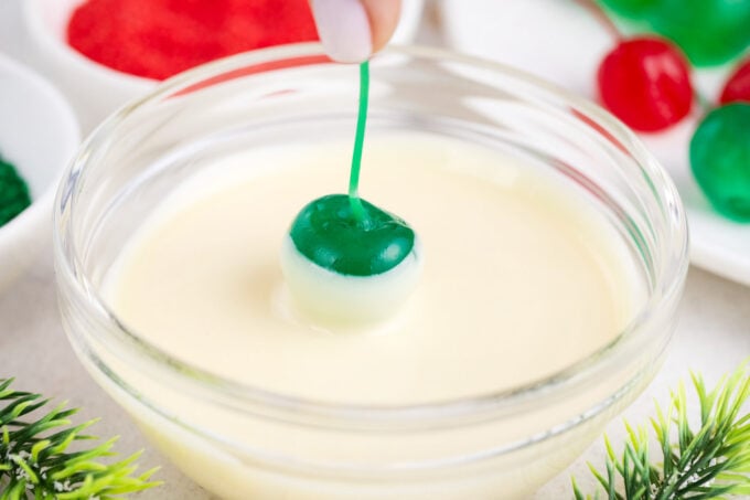 Dipping a green Maraschino cherry in white chocolate.