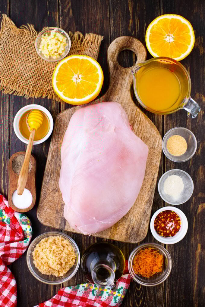 Overhead shot of oven roasted turkey breast with orange sauce ingredients in bowls on a wooden table.