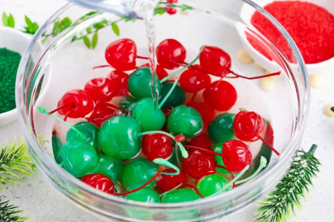 Pouring vodka over a bowl of green and red Maraschino cherries.