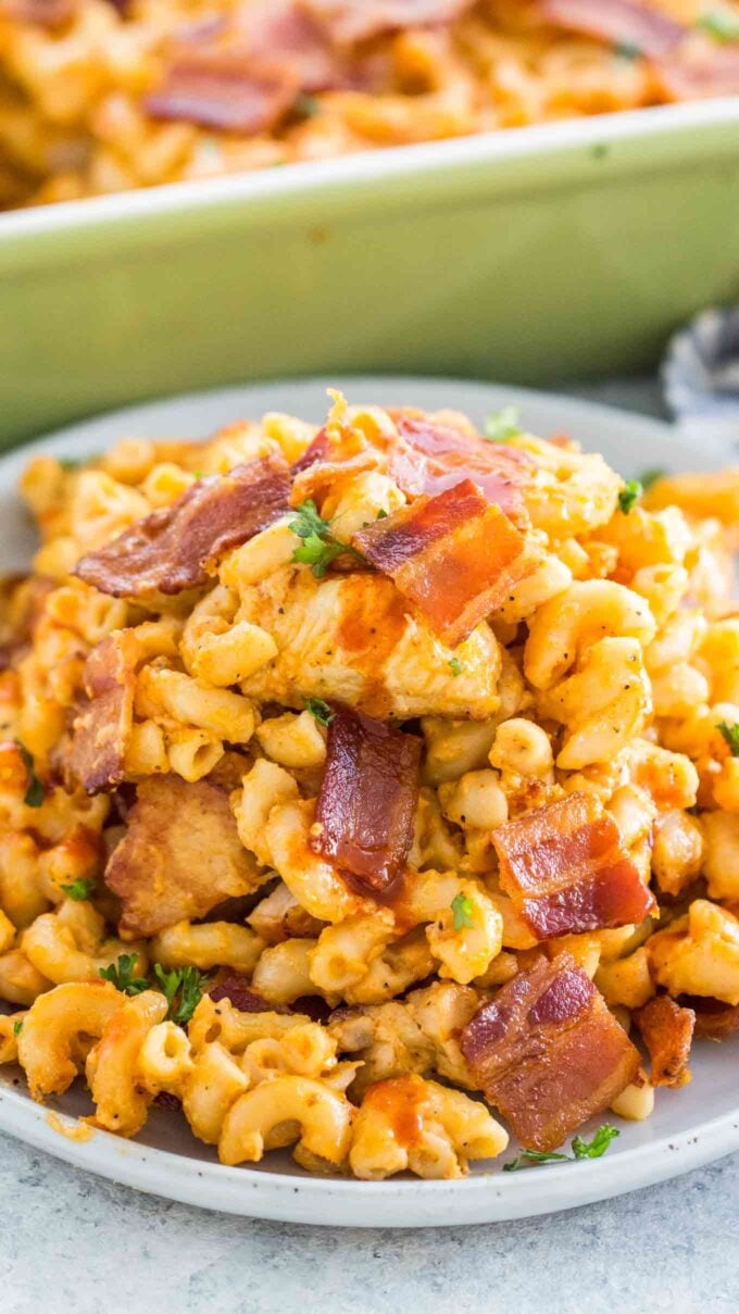 Creamy macaroni and cheese casserole with chicken and buffalo sauce topped with bacon on a plate