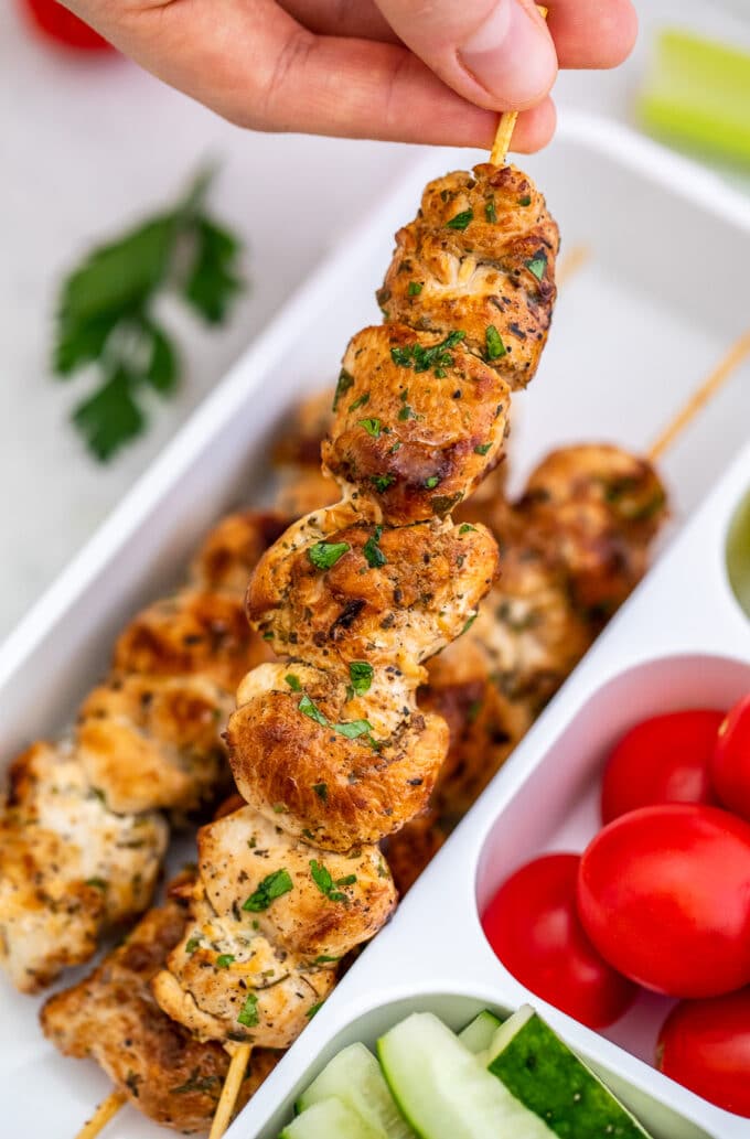 holding Italian Chicken Skewers in a lunch box with cucumbers and tomatoes