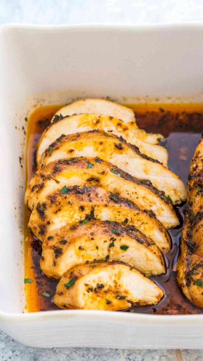 Sliced and seasoned chicken breasts baked in the oven in a white casserole dish