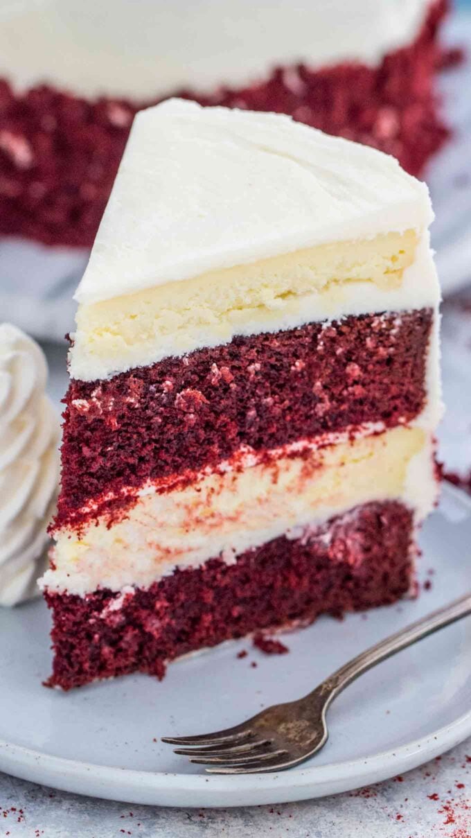 a slice of Red Velvet Cake Cheesecake with layers of red velvet cake, cheesecake, and cream cheese frosting