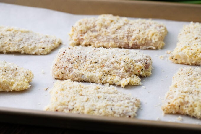 Tilapia fillets coated in breadcrumb mixture arranged on a baking dish.