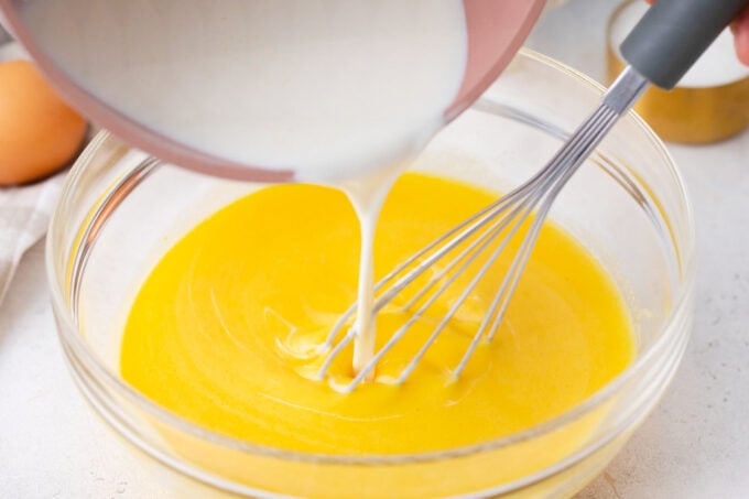 Adding warm cream to a bowl of whisked egg yolks.