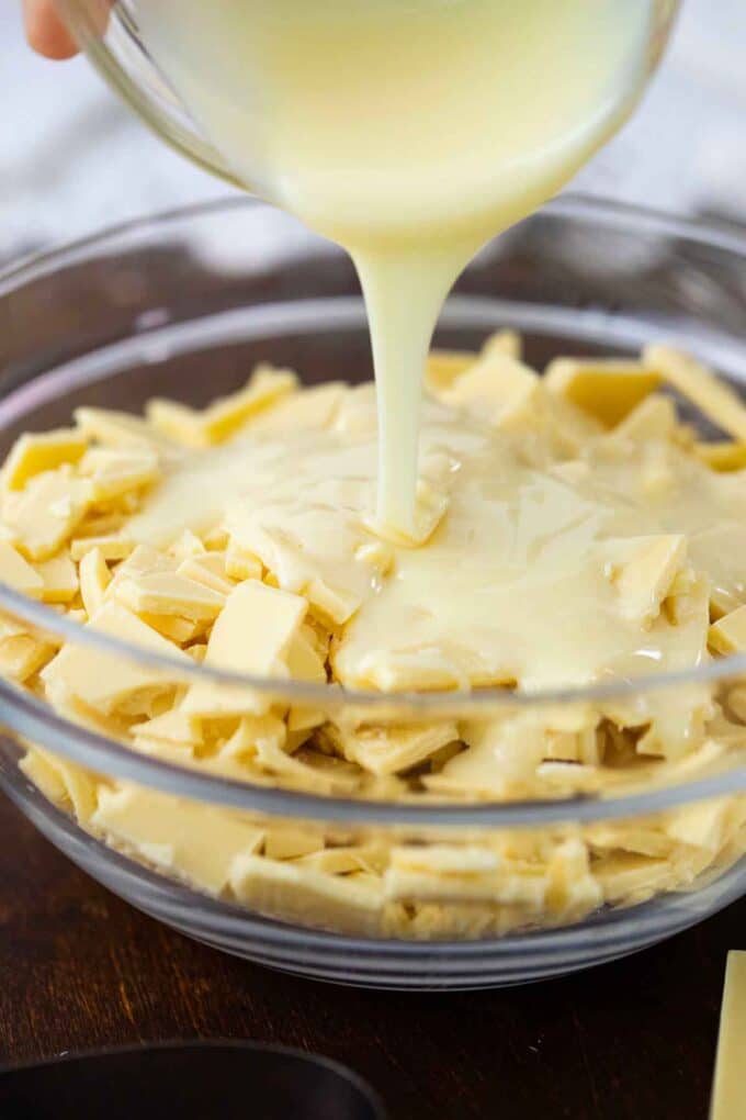 adding condensed milk to a bowl of chopped white chocolate