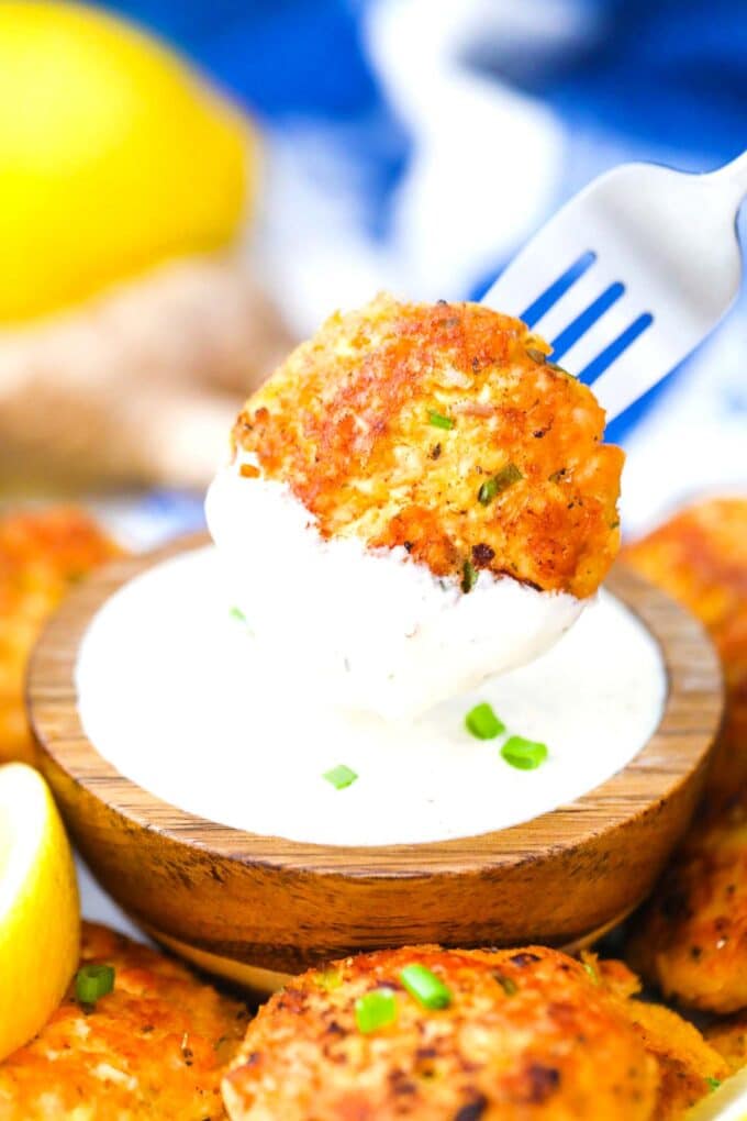 dipping a salmon cake in a white sauce