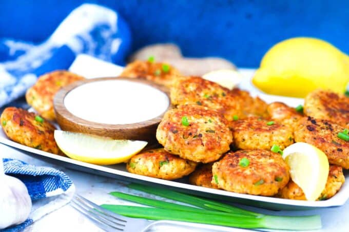 a serving plate with salmon patties white sauce and lemon wedges