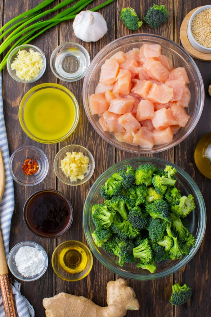 Overhead shot of chicken and broccoli recipe ingredients in bowls on a wooden surface.