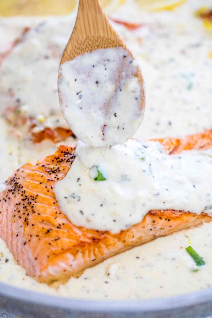 pouring homemade creamy lemon parmesan sauce on a piece of salmon