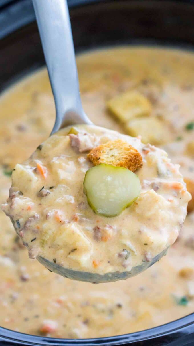 Creamy cheeseburger soup garnished with sliced pickles and crotons