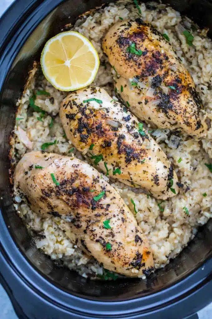 Cooked boneless chicken breast over brown rice in a slow cooker.