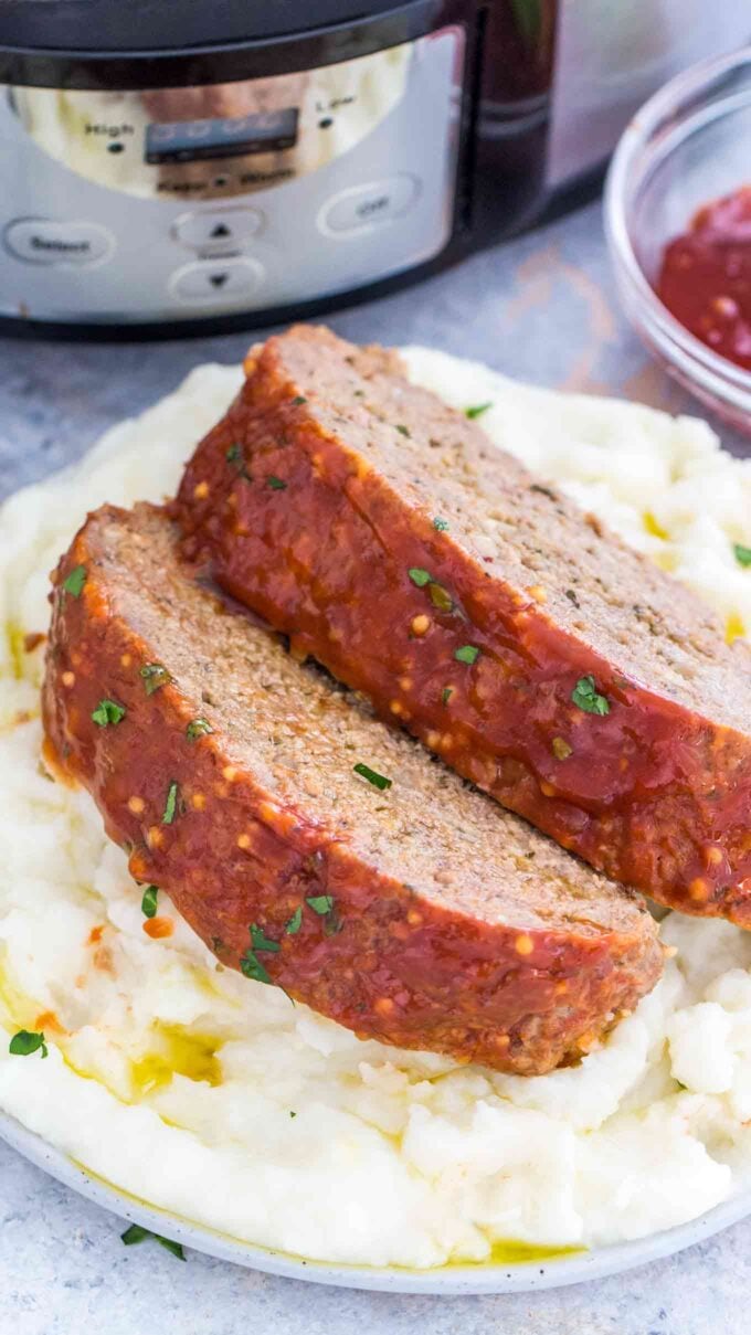 Sliced slow cooker meatloaf over mashed potatoes on a white plate. 