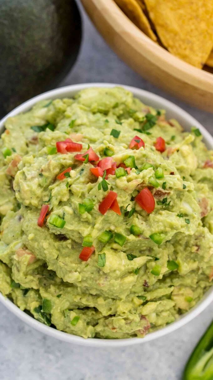 a bowl of Guacamole Recipe with an avocado and corn chips next to it