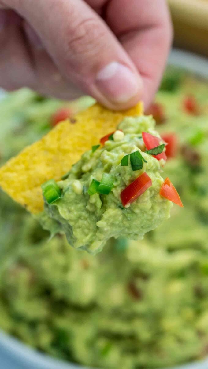 a hand holding a corn chip topped with Homemade Guacamole