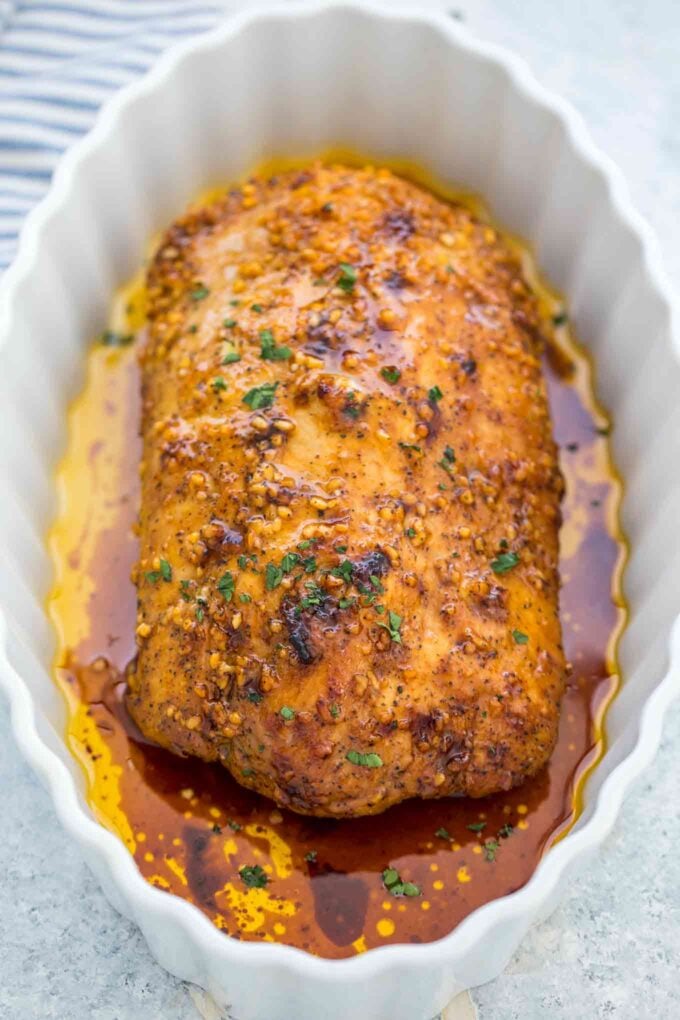 A whole piece of freshly baked pork loin toped with herbs in a white baking dish.