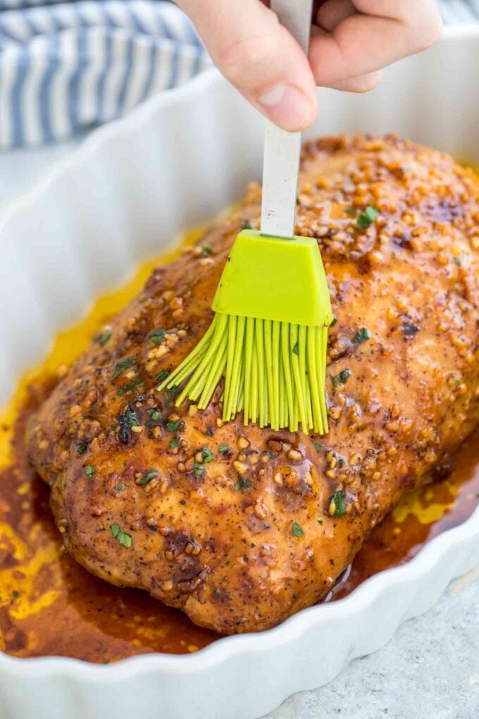 roasted pork loin brushed with garlic butter sauce and herbs top on a white baking dish. 