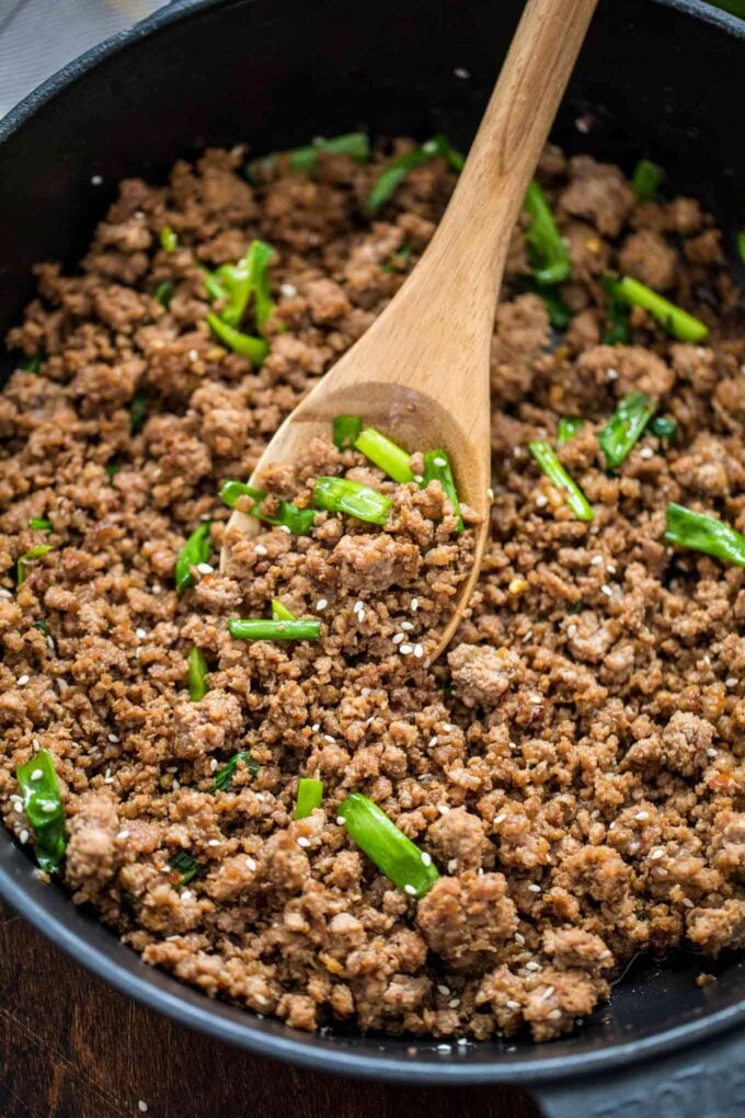 Ground beef cooked in a skillet with sliced green onion and sesame seeds.