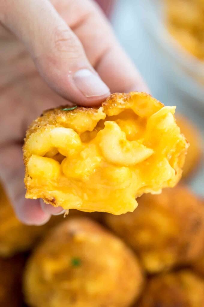 a hand holding a fried mac and cheese ball with oozing melted cheese