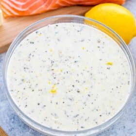 a bowl with creamy sauce for salmon with raw salmon on a cutting board and lemon next to it