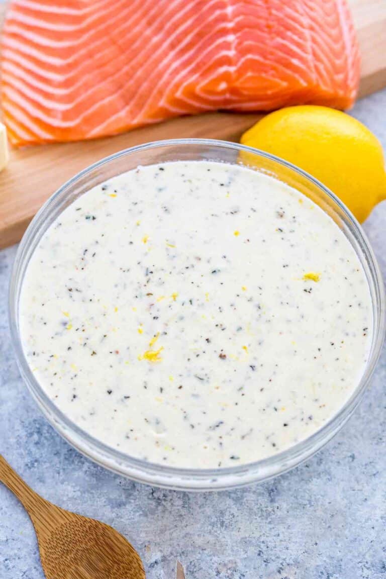 a bowl with creamy sauce for salmon with raw salmon on a cutting board and lemon next to it