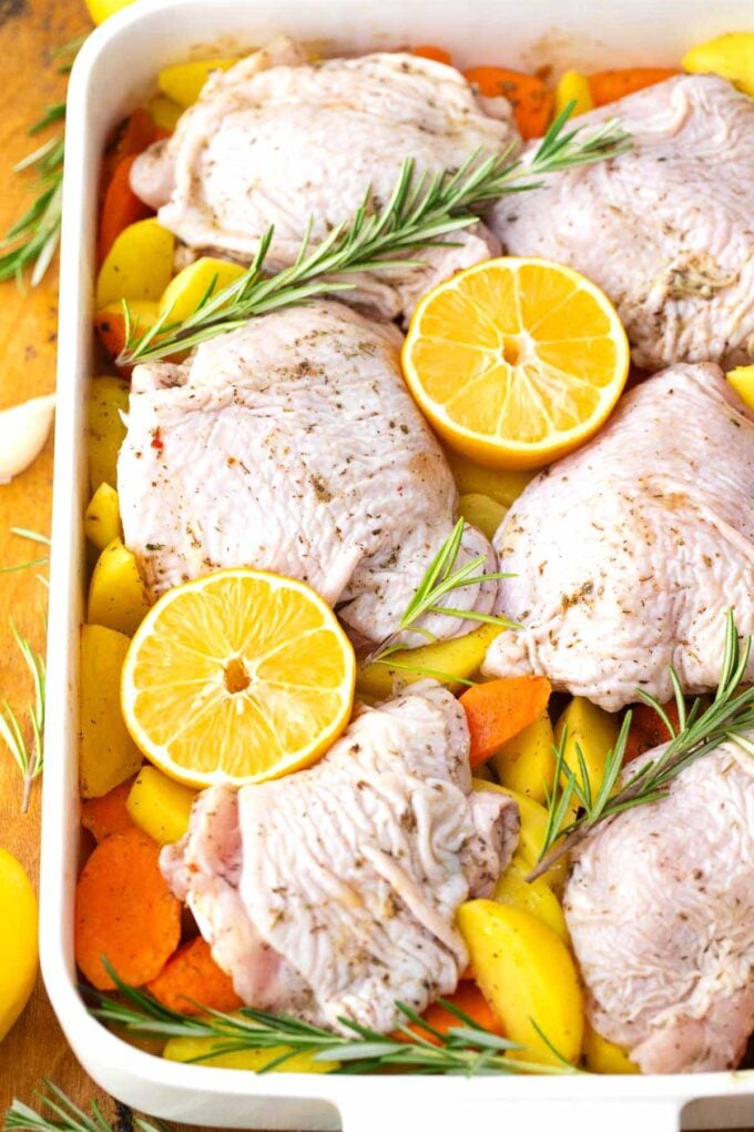 Chicken thighs on top of carrots and potatoes in a baking dish before baking.